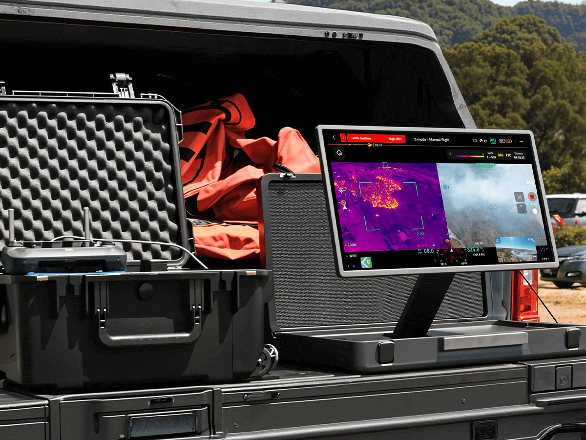 A Briefcase Portable TV (portable monitor) on a truck tailgate displays split-screen thermal and real-time drone footage for field operations.