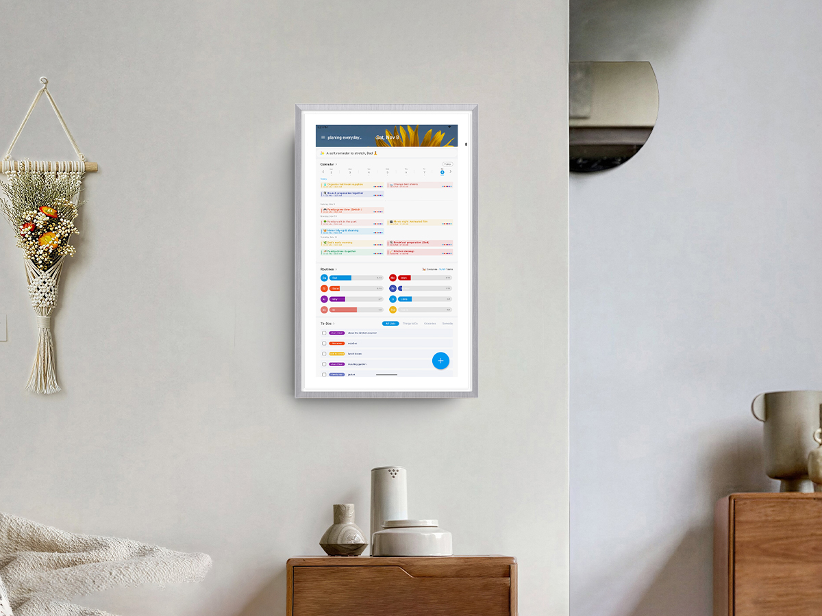 A wall-mounted Digital Calendar displaying a detailed family schedule, routines, and a to-do list in a living room setting.