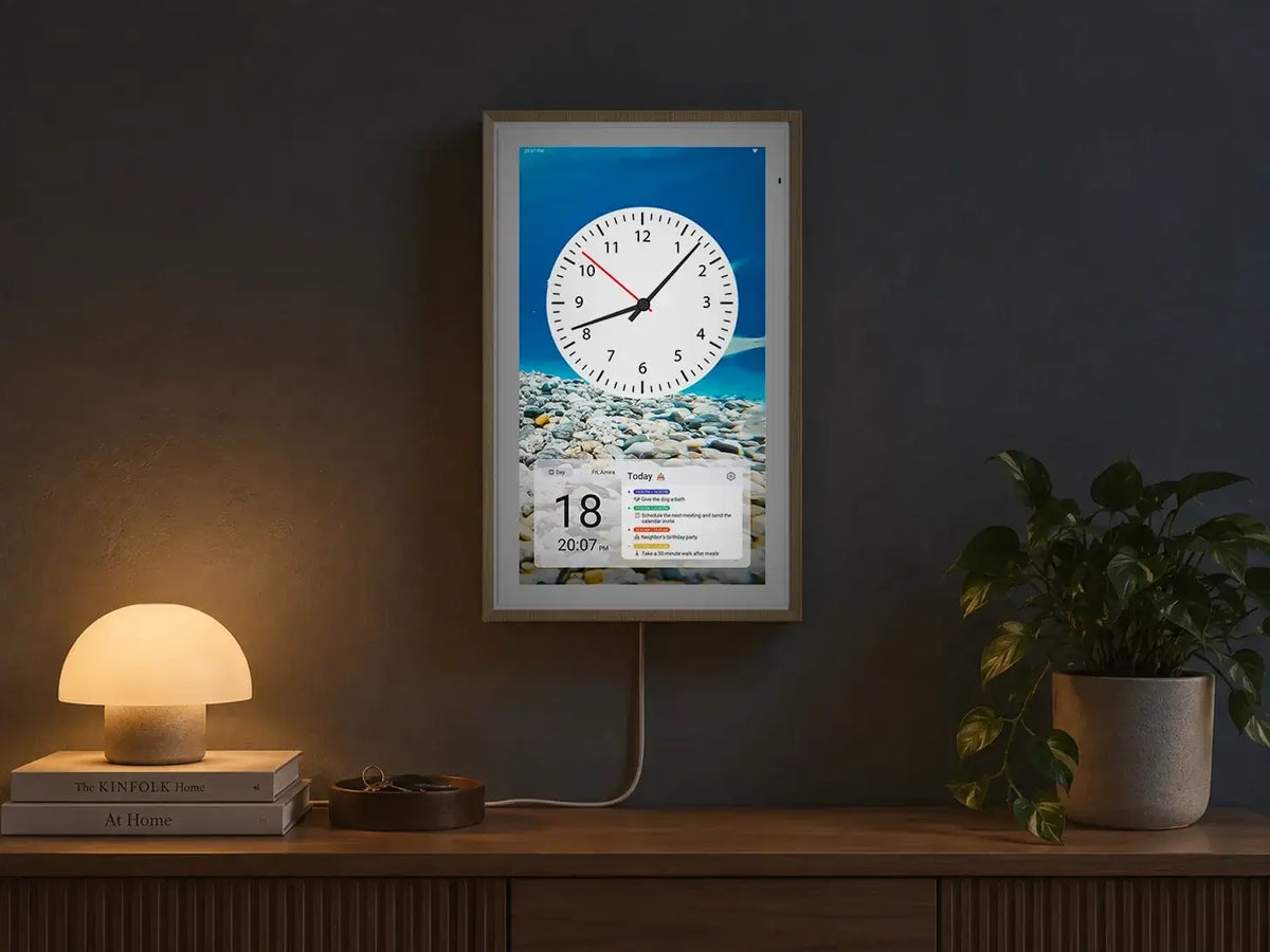 A wall-mounted Digital Calendar displaying a clock face and today's schedule, placed above a wooden sideboard with a lamp and a potted plant.